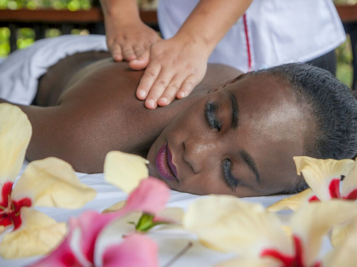 A person receiving a relaxing back massage, surrounded by flowers, while lying on a white surface.